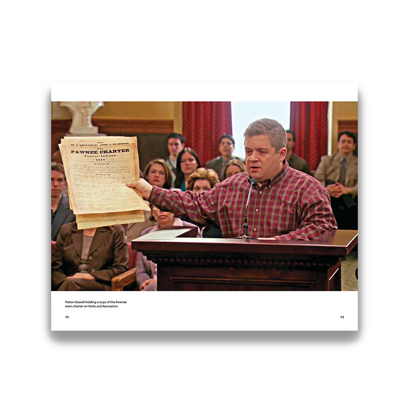Man in a courtroom holding a document, with a group of people seated behind him.