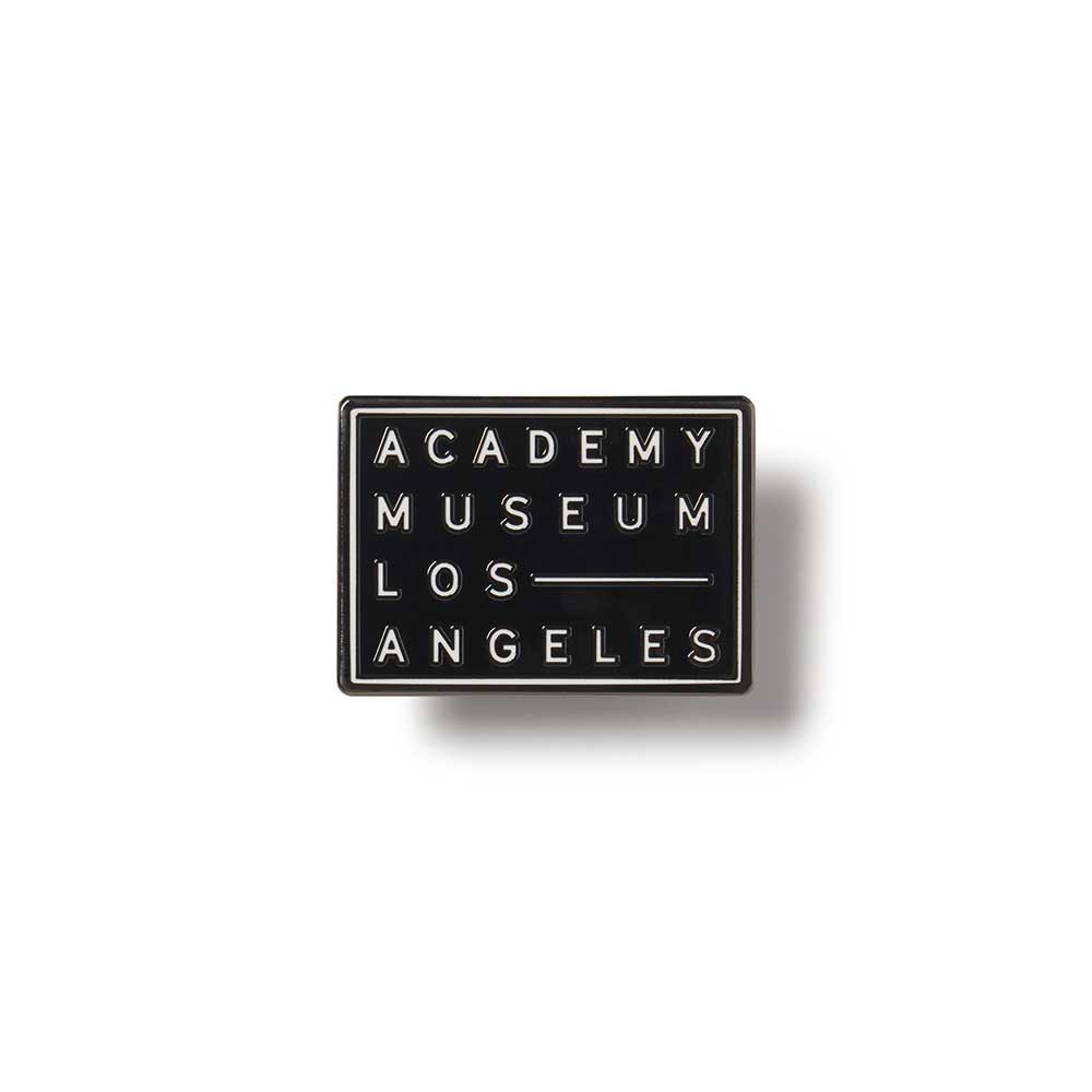 Black square lapel pin with 'Academy Museum Los Angeles' text on a white background
