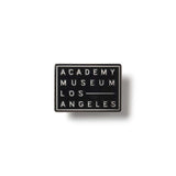 Black square lapel pin with 'Academy Museum Los Angeles' text on a white background