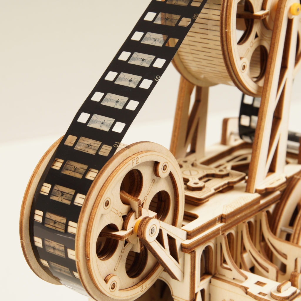 Wooden mechanical model of a film projector with film reels and film strip.