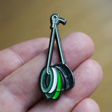 Enamel pin of a green and white object held between two hooks on a blurred background