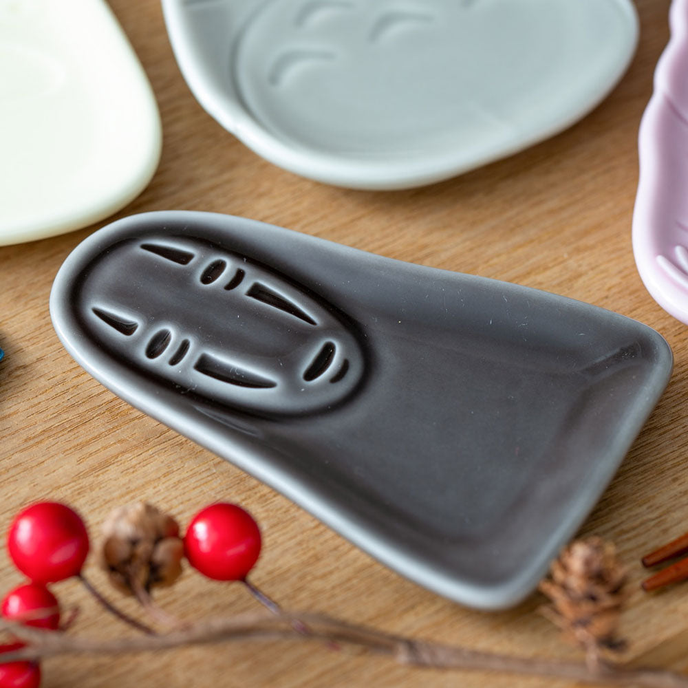 Gray ceramic dish with decorative patterns on a wooden surface with red berries and branches. Ceramic condiment dish in the shape of No Face from Studio Ghibli's Spirited Away.