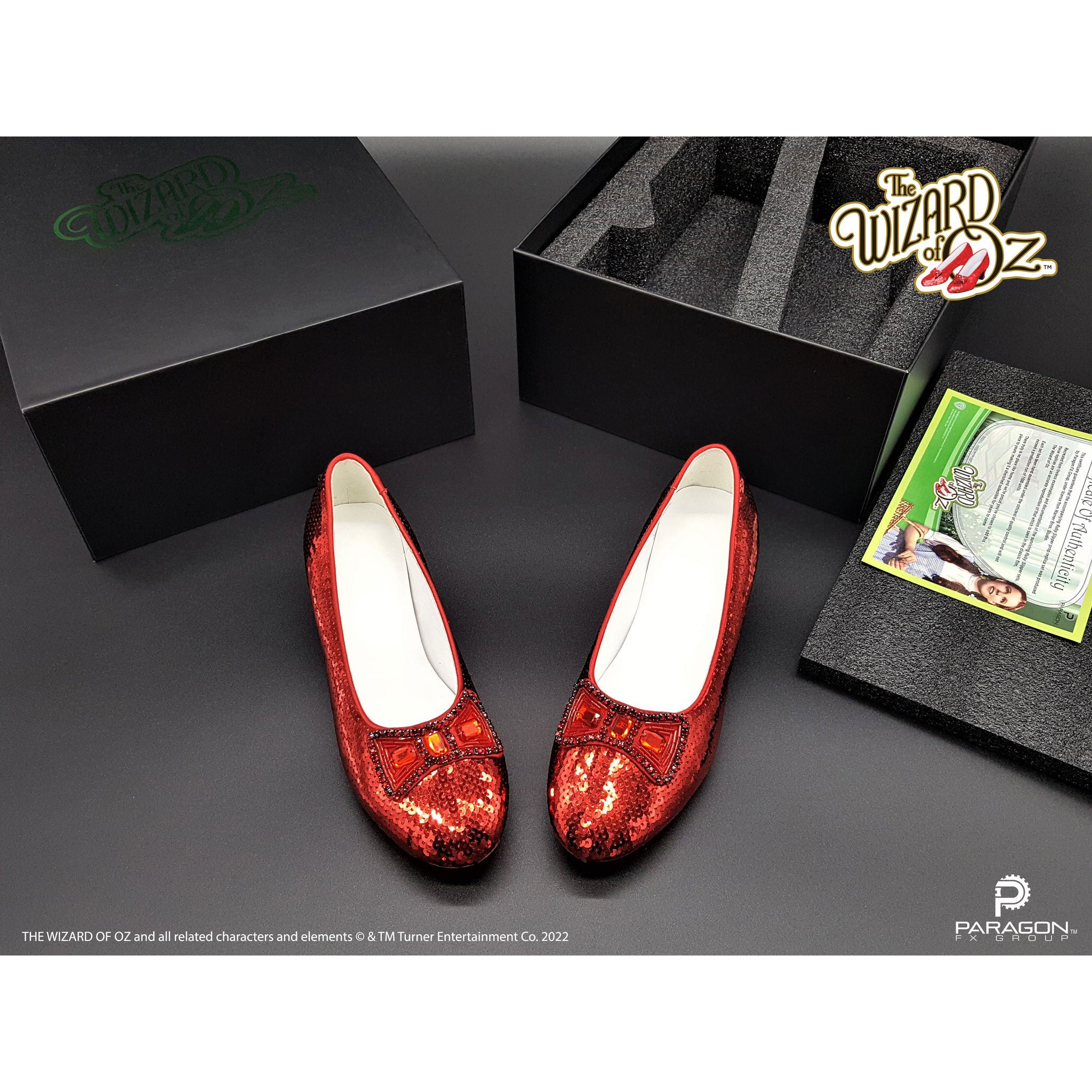 Red glittery shoes with white soles on a gray surface, featuring 'The Wizard of Oz' branding. image shows collectors numbered box and certificate of authenticity. Movie Prop Authentic Museum Quality Replica Dorothy's Ruby Slippers from The Wizard of Oz