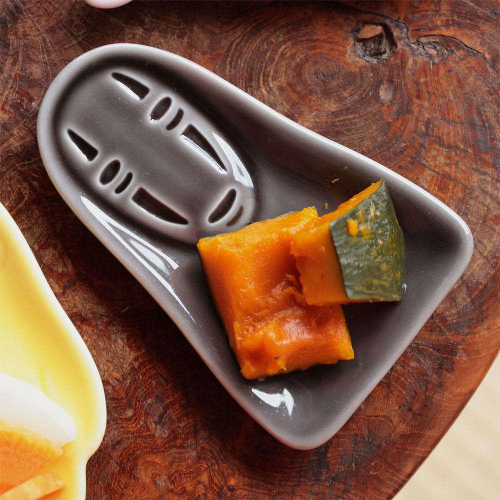 Gray ceramic dish with sliced pumpkin on a wooden surface. Ceramic condiment dish in the shape of No Face from Studio Ghibli's Spirited Away.
