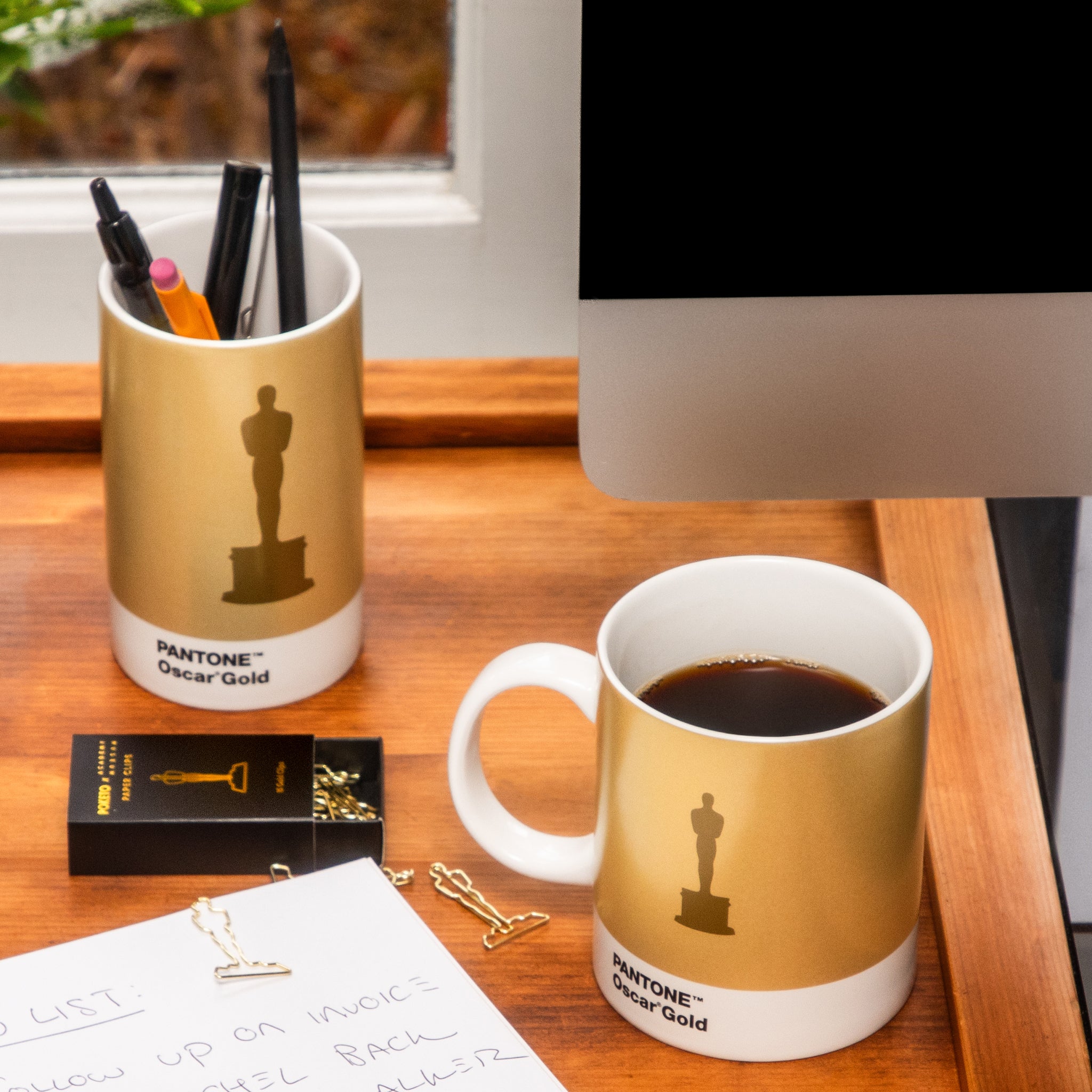 PANTONE Oscar Gold mug with a cup of coffee on a desk, next to a pen holder and computer. ceramic pencil cup holder Oscar Statue