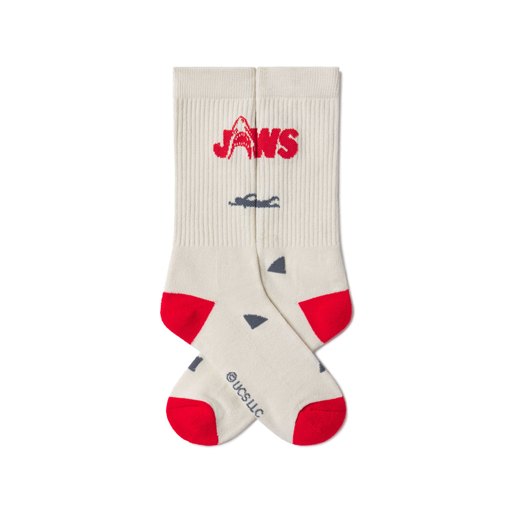 Beige socks with red accents and 'JAWS' logo on a white background. JAWS 50th ANNIVERSARY | ACADEMY MUSEUM