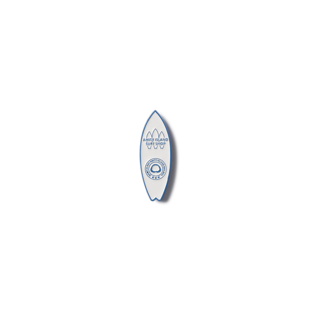 Small blue and white surfboard-shaped lapel pin on a white background featuring the Amity Island Surf Shop[ Logo from the movie JAWS 50th Anniversary Exclusive Lapel Pin Academy Museum Store Los Angeles.