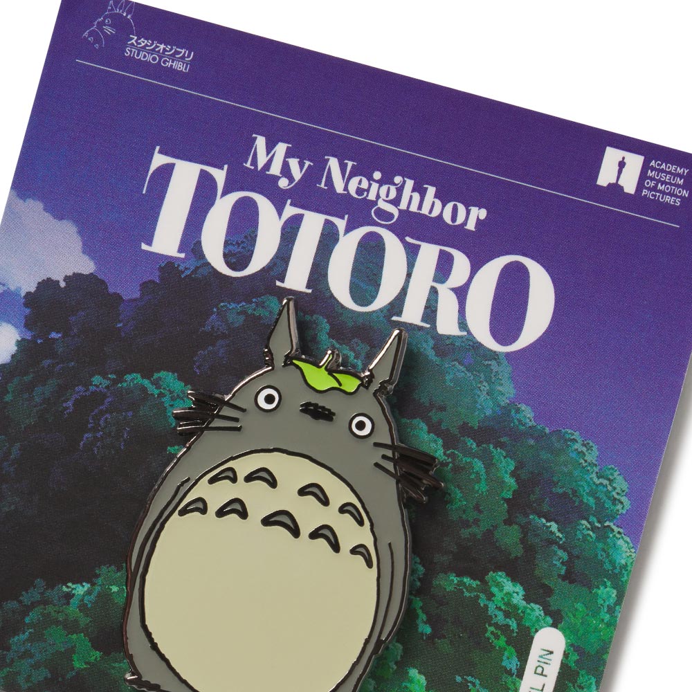 An enamel pin with the character Totoro from My Neighbor Totoro animated movie, placed on a card with the movie's title and artwork.