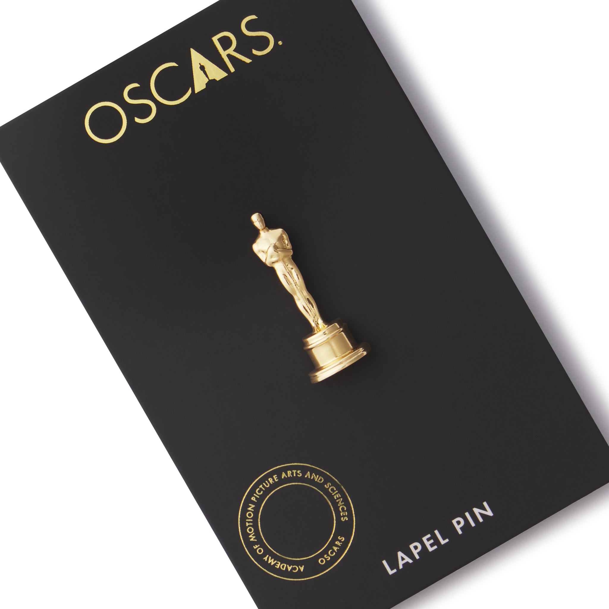 An image of a gold-plated brass Oscar statuette lapel pin presented on a black card with 'OSCAPS' text and a description of the pin as a 'LAPEL PIN'.