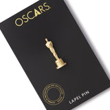 An image of a gold-plated brass Oscar statuette lapel pin presented on a black card with 'OSCAPS' text and a description of the pin as a 'LAPEL PIN'.