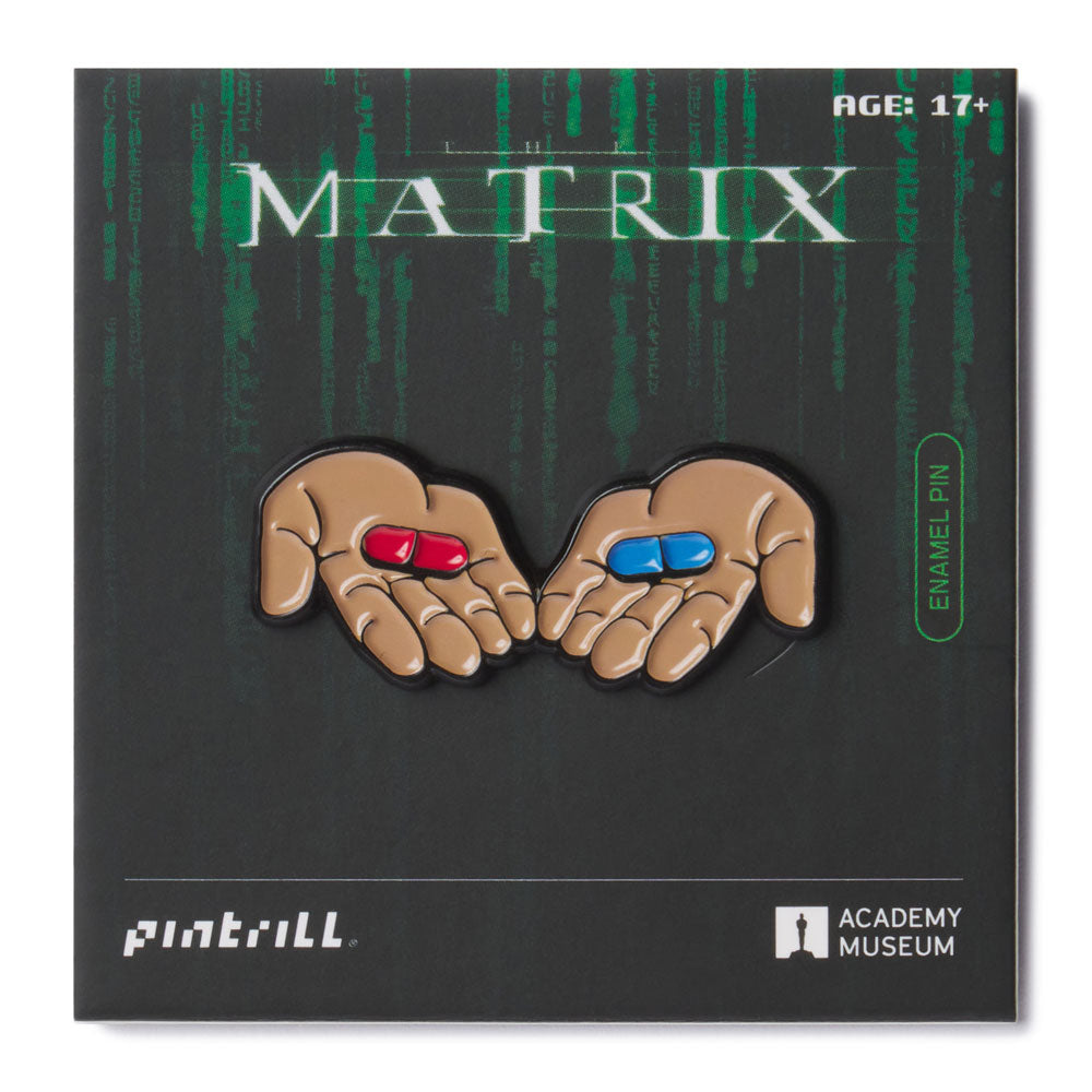 Enamel pin of hands holding red and blue pills from 'The Matrix' on a black background with 'Pintrill' and 'Academy Museum' logos.