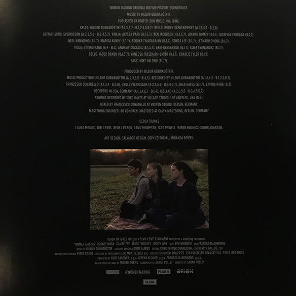 Back cover of a music album with a photo of three people sitting on grass and credits.