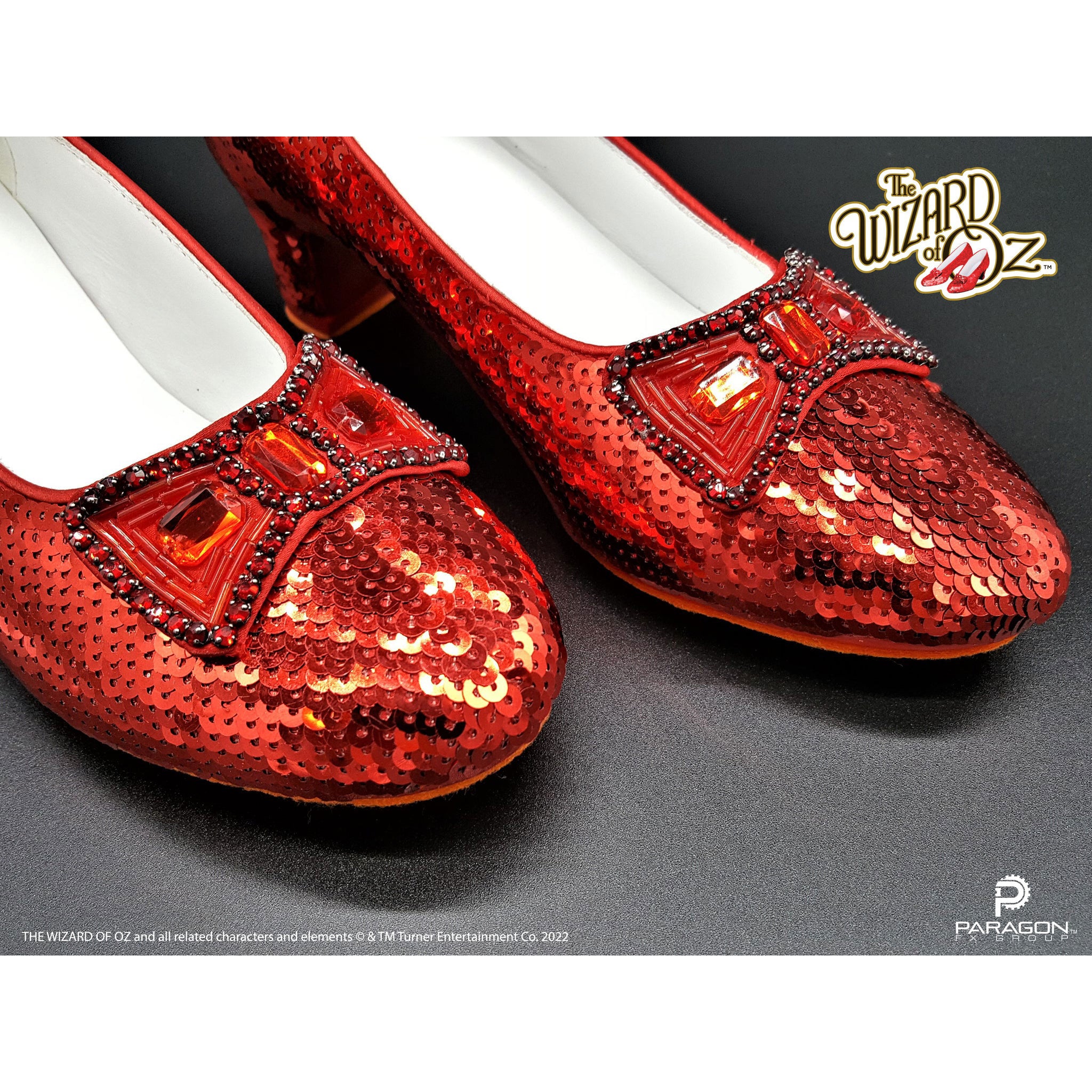 Dorothy's Ruby Slippers from The Wizard of Oz Red sequin shoes with decorative elements on a gray background, featuring 'The Wizard of Oz' branding.