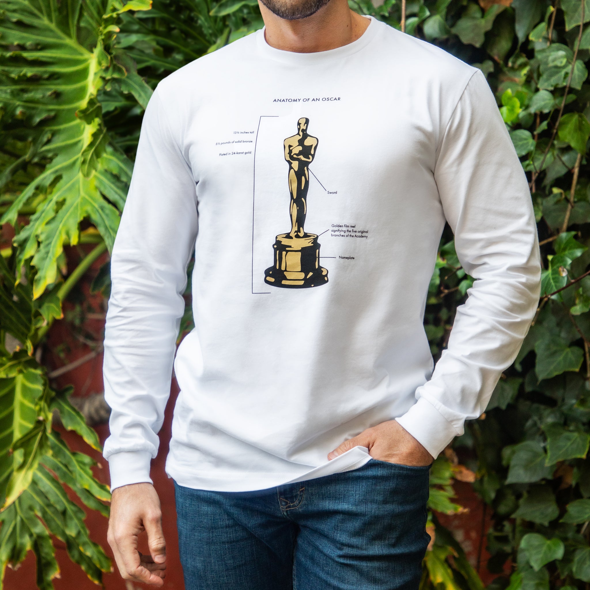 Person wearing a white long-sleeve shirt with an illustration of an award statue against a green leafy background