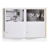 Open book showing two black and white photographs, one of a room and one of a forest, on a white background sceens from the movie The Lobster (2015)