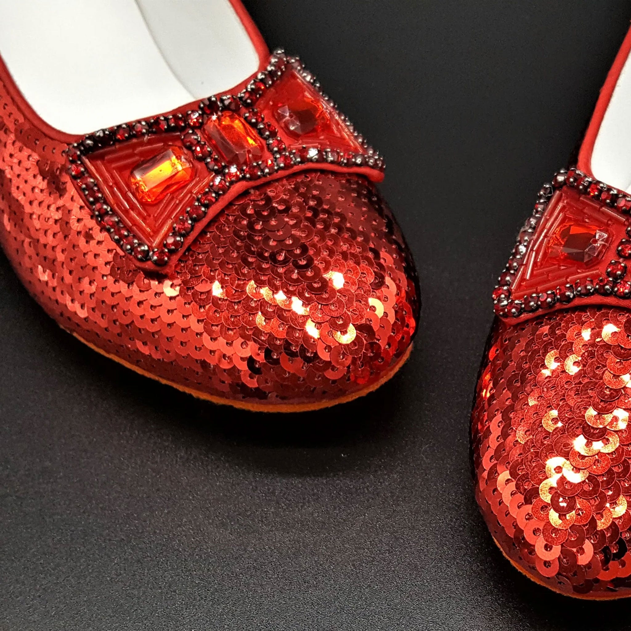Red sequin shoes with embellishments on a black background. Movie Prop Authentic Museum Quality Replica Dorothy's Ruby Slippers from The Wizard of Oz