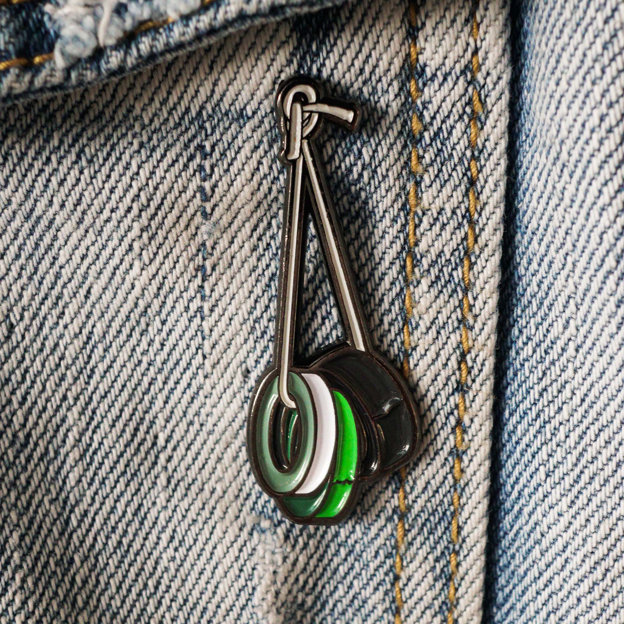 gaffing tape Enamel pin with green, white, and black design on denim fabric