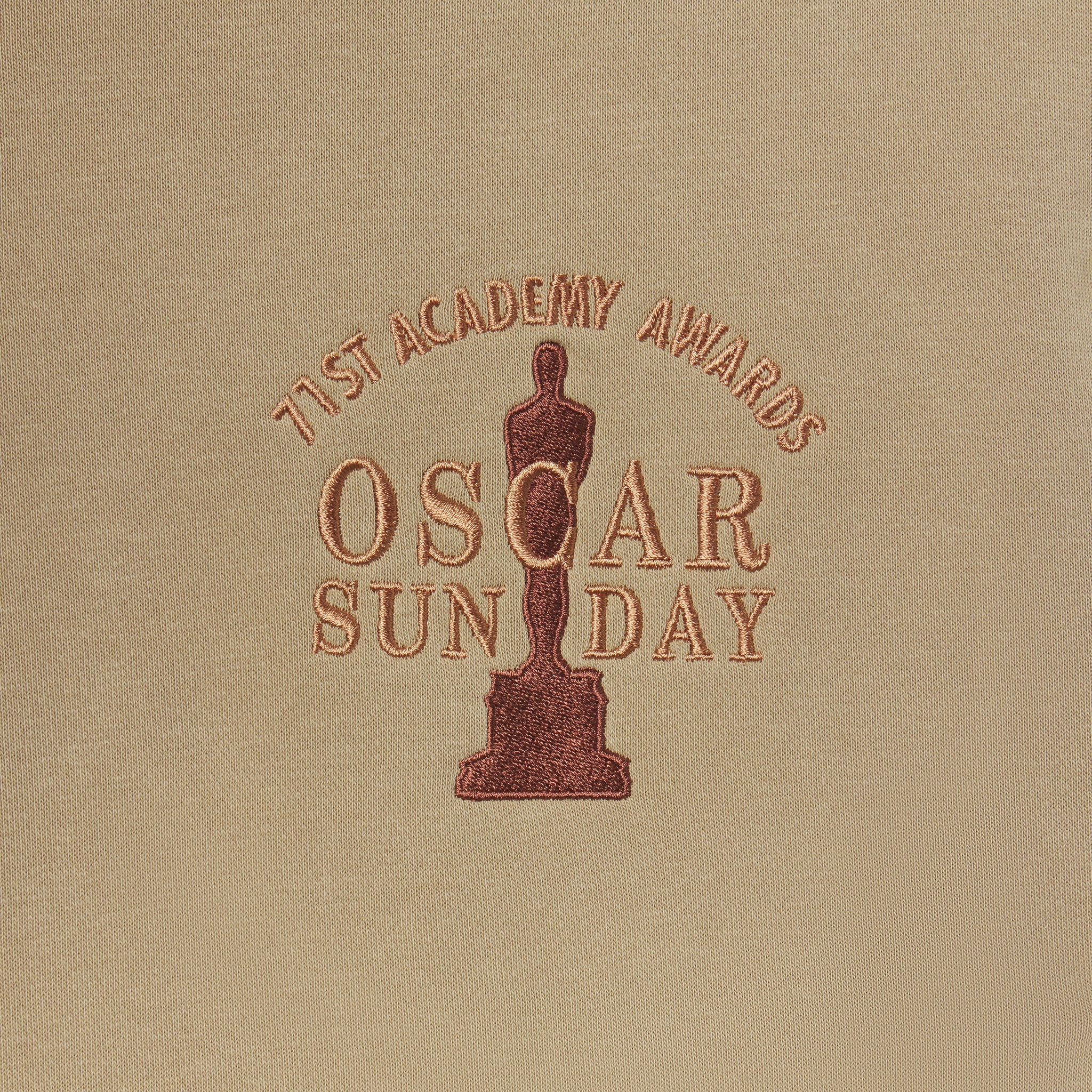 Embroidered Oscar statue and text on a beige fabric background