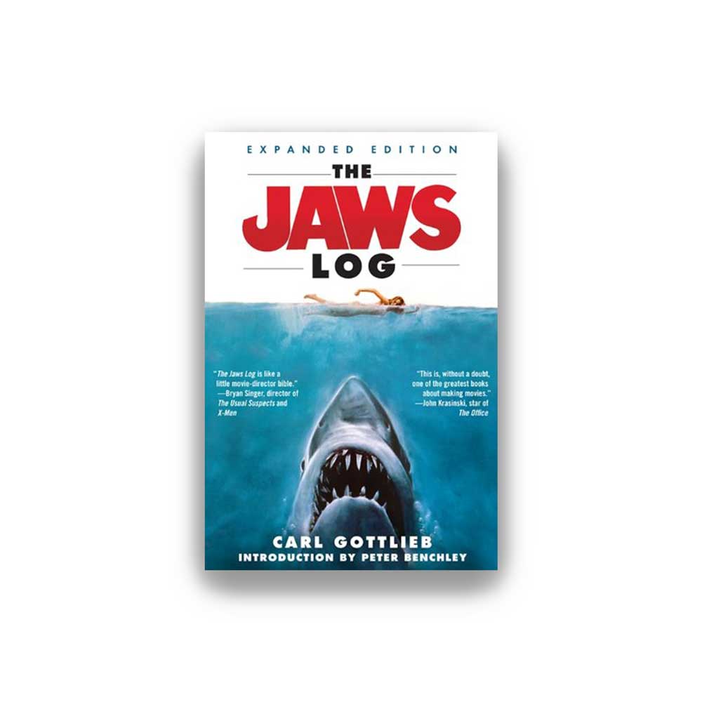 This image displays the cover of "The Jaws Log: Expanded Edition" by Carl Gottlieb, featuring a striking depiction of the iconic shark, Jaws, breaking the surface. The book’s title is prominently displayed at the top in bold, red letters, with a white subtitle underneath, stating "Shooting Script.