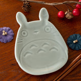 Grey ceramic dish shaped like a Studio Ghibli Totoro character on a wooden surface with decorative elements.