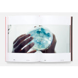 Open book showing a page with a hand holding a petri dish containing blue and white colonies.