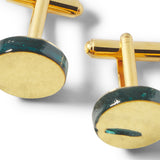 Gold cufflinks with green accents on a white background
