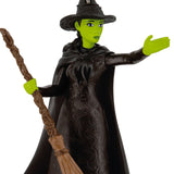Toy figure of a witch with green skin, black hat, and cloak holding a broomstick on a white background from the movie Wicked