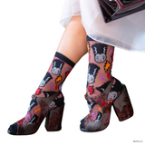 Colorful socks with cartoon character design worn with high-heeled shoes on a white background. Elevate your fall style with the Bride of Frankenstein Shimmer Sheer Crew Sock. A perfect blend of spooky glam and comfort, featuring a kawaii design and rich colors.