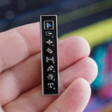 Bar-shaped metal badge with symbols held in a hand against a blurred colorful background
