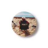 Button badge with film director Agnes Varda on a beach, wearing a jacket with 'AGNES V.' text.