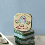 Stack of Jane Austen-themed tins with decorative labels on a light blue background. Experience the refreshing taste of Jane Austen's Pride and Peppermints! These charming mints are ideal for a quick pick-me-up anytime, anywhere.