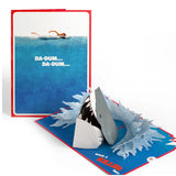 Pop-up card with shark attack design and text 'DA-DUM... DA-DUM...' on a white background JAWS 50th anniversay greeting card