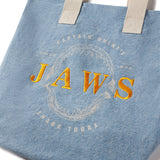 Blue tote bag with 'JAWS' embroidery on a white background Celebrate 50 years of JAWS with this exclusive tote bag! Made from premium denim, it features an embroidered logo and captures the spirit of Captain Quint.