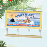 Ornament resembling a 'Amity Island' billboard with a woman, shark, and text on a Christmas tree.
