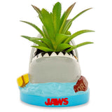 Jaws-shaped planter with a plant on a white background. Transform your decor with the Jaws Shark Ceramic Mini Planter! This adorable piece showcases a succulent, combining movie magic with effortless style.