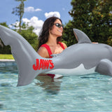 a woman standing in a pool holding the tail of the inflatable shark pool noodle with the logo JAWS printed in red