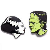 Two enamel pins of a woman and a man with a green face on a white background.Bride of Frankenstein and Frankenstien profile image pins that glow in the dark Halloween Official Universal Studios Monsters