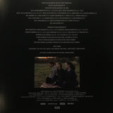 Back cover of a music album with a photo of three people sitting on grass and credits.