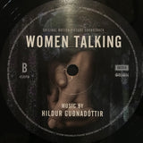 Vinyl record label for 'Women Talking' soundtrack with a hand holding an ear design.