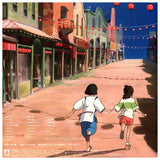 Two children holding hands on a colorful street with buildings and lanterns. Scene from Spirited Away