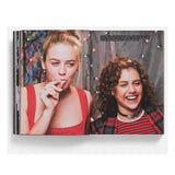 Open book showing two people with a festive background photo of Cher and Tai from the movie Clueless