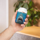 Hand holding a can with a shark design on a blue background, blurred indoor setting