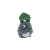 Plush toy of a small grey  Studio Ghibli totoro holding a green leaf on a white background