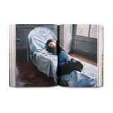 Open book showing a Sofia Coppola lying on a bed with blue bedding in a room with wooden floors and a window.